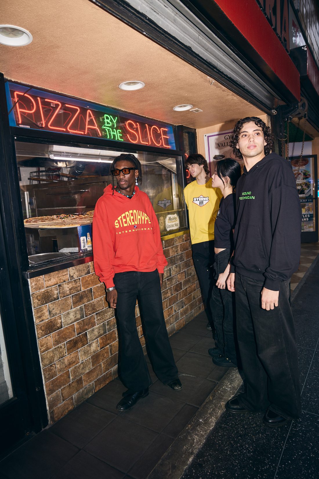 Model in red STEREOHYPE INTERNATIONAL hoodie in front of pizza-by-the-slice neon